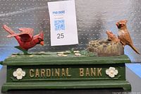 Side view of the cast iron bank with two cardinal birds and nest, green base labeled 'Cardinal Bank' with flowers.