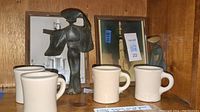 Photo showing two vintage cream color Wallace China coffee cups, two cast iron statues of human figures, and two 10x8 inch wooden rocket photo frames.
