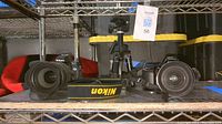 Wide shot of Nikon cameras on shelf with tripod in background, showing cameras with lenses attached and Nikon strap in front.