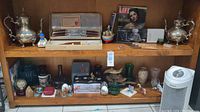 Full view of several antique and vintage items on wooden shelf including silver plated teapots, collectible figurines, and vintage cutlery set in box