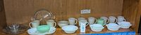 Wide view of entire set showing mugs, plates, bowls, and glass pie plate arranged on shelving.
