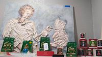 Display of brass reindeer, Christmas tree ornaments, blue bell, and boxed Christmas figurines in front of the painting