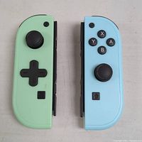 Front view of left pastel green and right pastel blue Nintendo Switch Joy-Con controllers placed side by side on a flat surface.