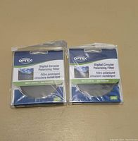 Top view of two sealed Optex Digital Circular Polarizing Filter packages in blue and green packaging.