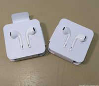 Two sets of white earbud-style wired headsets in plastic holders, showing earbud design and packaging.