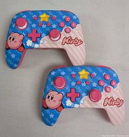 Two Kirby-themed Nintendo Switch wireless controllers shown from front, highlighting colorful button layout and graphical design.
