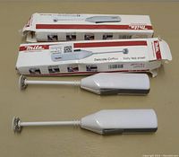 Two Mita electric milk frothers outside their boxes, showing the white and grey frother design and whisk attachments.