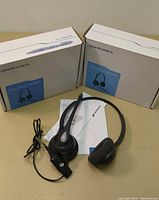 One unboxed Plantronics SupraPlus HW261N wired headset with single cushioned ear pad and boom microphone displayed with two unopened boxes in the background.