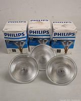 Three Philips halogen light bulbs with their original packaging showing the product details such as wattage and lifespan.