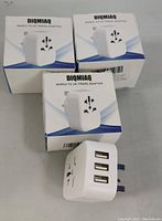 Three boxed DIQMIAQ World to UK Travel Adapters and one adapter showing 3 USB ports and UK plug