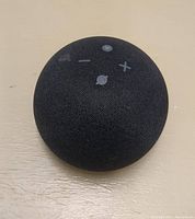 Black Amazon Echo Dot 4th Gen speaker top view showing fabric covering and control buttons.