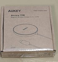 Front view of unopened sealed cardboard box packaging of Aukey Aircore 15W Magnetic Wireless Charger with printed illustration and details.