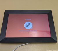 Front view of digital picture frame powered on, displaying welcome screen with prompt about power disconnection.