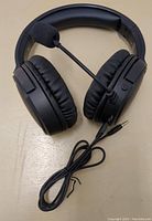 Black wired over-ear headphones with cushioned ear pads, adjustable headband, microphone boom attached to left ear cup, and 3.5mm audio cable on a beige surface.