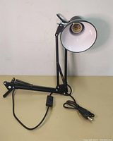 Black adjustable desk lamp with clamp base, conical lamp head with white interior, inline power switch, and power cord visible.