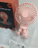 Pink handheld fan with flexible legs, USB cable and packaging box visible