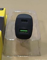 Close-up image of black USB car charger showing one USB-C port and one green USB-A port in plastic packaging.