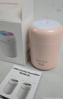 Photo showing the Sonex H2O pink mini humidifier with its original box and user manual laid out on a grey surface.