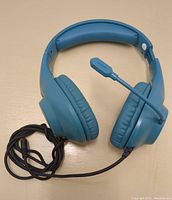 Front view of blue Phoinkas H-7 wired headphones with cushioned ear pads and attached microphone, laid flat with cable coiled.