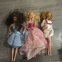 Two vintage Barbie dolls lying on wooden floor; one dressed in pink with blonde hair, the other in blue with brown hair.