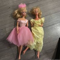 Top view of two 1966 vintage Barbie dolls, one in pink ballerina dress and one in yellow nightgown, placed on wood floor.