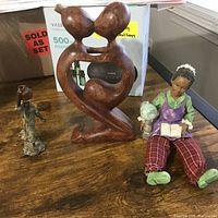 Photo of three items on table showing wooden carving, elderly figure and metal figure.