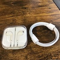 Apple EarPods with Lightning connector in clear plastic case and white Lightning cable coiled beside it, on wooden surface.