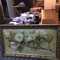 Framed floral painting showing white magnolia flowers with green leaves in an ornate gold frame.
