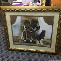 Full view of framed painting showing two young girls whispering, set in ornate gold frame with matting.