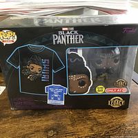 Packaged Marvel Studios Black Panther Funko Pop collectible with visible branding and T-shirt size sticker, displayed on a table.