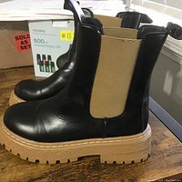 Side view of boys black rain boots showing tan elastic side panels and thick tan lug soles.