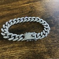 Silver-tone bracelet curb chain style fully covered with clear stones on wooden surface.