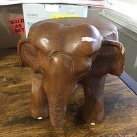 Front view of the brown wooden elephant carving showing details of the ears, eyes, and some white paint chipping.