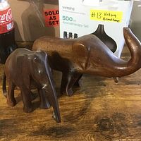 Two hand carved wooden elephant figurines on a wooden surface, showing the size and details of the carvings.