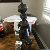 Full view of the wooden African statue showing broken arm and balancing pot on head.