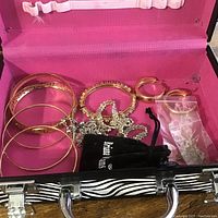 Open zebra print jewelry box interior showing various bangles, a necklace, pouches, and earrings inside.