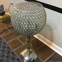 Full view of the crystal ball table lamp showing the spherical lampshade made of clear circular crystals on metal rings and shiny chrome base with power cord.