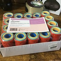 Tray of 144 orange Diane magnetic hair rollers with blue and yellow inner rings, with packaging label describing the product.