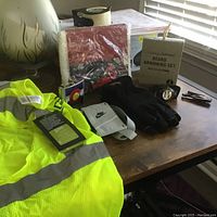 Wide view of all items on wooden table showing safety vest, gloves, grooming set, watch, and Nike accessories
