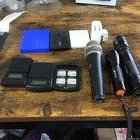 Full view of all items arranged on wooden table including blue device, Alcatel router, Zoom device, 3 scales, microphone, 2 flashlights, and white wired device.