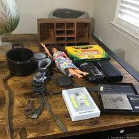 Wide view of lot showing cast iron pot, wooden organizer, doll, markers, cassette recorder, USB cable, spoon, and light switch.