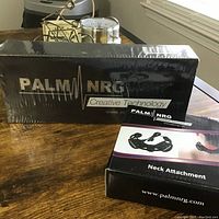 Photo showing Palm NRG Creative Technology device and Neck Attachment sealed in their original boxes on a wooden surface.