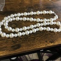 Pearl necklace laying on wooden surface showing entire strand with varied size pearls.