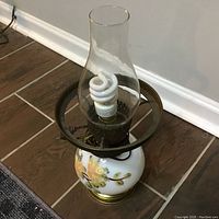 Top-down angled photo of vintage floral glass lamp showing the glass chimney, floral painted base and spiral CFL bulb inside.