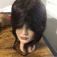 Front view of the black synthetic practice wig on the wig head showing hair texture and style.