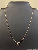 Full length view of the gold chain necklace displayed against black backdrop showing entire necklace with heart pendant at center.