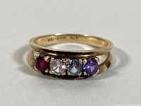 Close up view of the gold ring displaying four different colored stones: red, light blue, darker blue, and purple on a yellow gold band.
