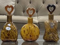 Front view shows three Murano blown glass bottles with heart-shaped stoppers in amber and brown mottled colors, two with original tags.