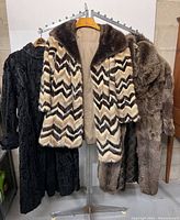 Three fur coats displayed on rack: chevron pattern center, black coat left, brown coat right