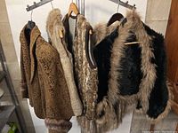 Shows five vintage ladies' rabbit fur jackets and vests hanging side by side, varying shades of brown and black with different fur textures.